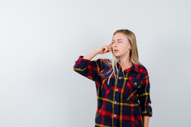 Kostenloses Foto porträt der jungen dame, die in der denkenden pose im karierten hemd steht und nachdenkliche vorderansicht schaut