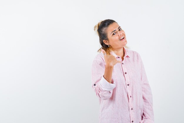 Porträt der jungen Dame, die Telefongeste im rosa Hemd zeigt und fröhliche Vorderansicht schaut