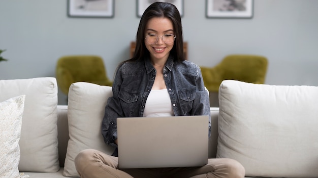 Porträt der jungen Frau, die einen Laptop auf der Couch hält