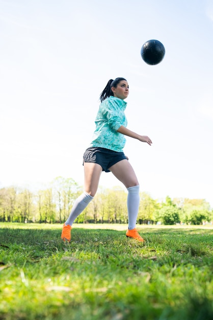 Porträt der jungen Frau, die Fußballfähigkeiten übt und Tricks mit dem Fußball macht