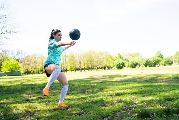 Porträt der jungen Frau, die Fußballfähigkeiten übt und Tricks mit dem Fußball macht