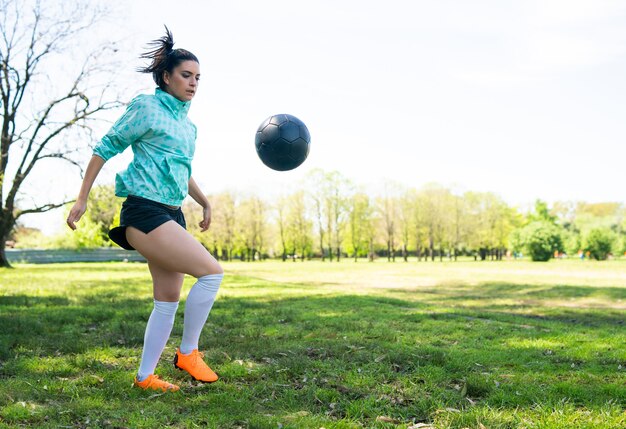 Porträt der jungen Frau, die Fußballfähigkeiten übt und Tricks mit dem Fußball macht