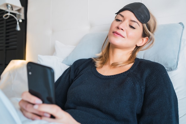 Porträt der jungen Frau, die ihr Handy benutzt, während sie auf dem Bett im Hotelzimmer liegt. Reise- und Lifestyle-Konzept.