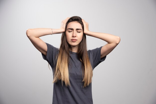 Porträt der jungen Frau, die ihren Kopf berührt, der über grauem Hintergrund aufwirft.