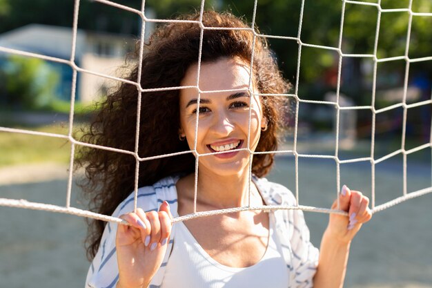 Porträt der jungen Frau, die neben einem Volleyballfeld im Freien aufwirft