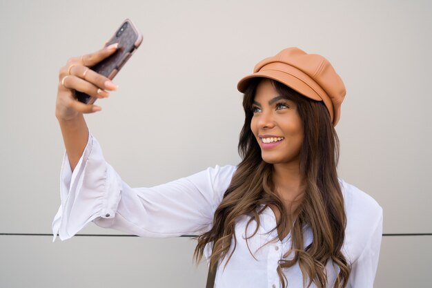 Porträt der jungen Frau, die Selfies mit ihrem mophilen Telefon nimmt, während sie draußen steht