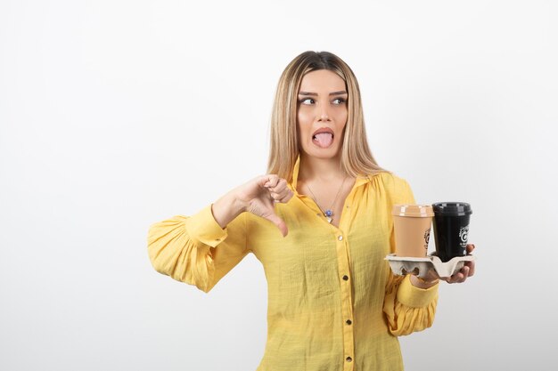 Porträt der jungen Frau, die Tassen Kaffee hält und Daumen nach unten gibt.