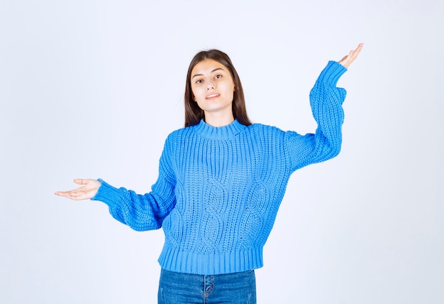 Porträt der jungen Frau in der blauen Strickjacke, die auf Weiß steht.