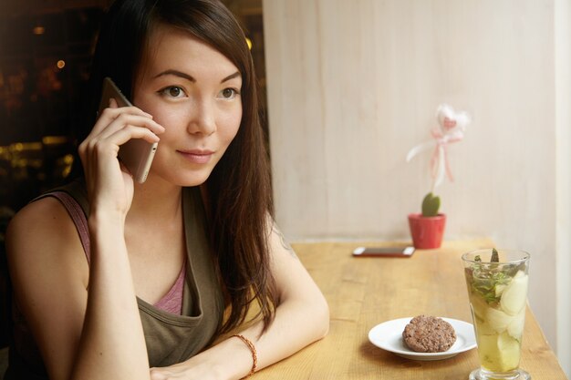 Porträt der jungen Frau mit brünettem Haar unter Verwendung des Telefons