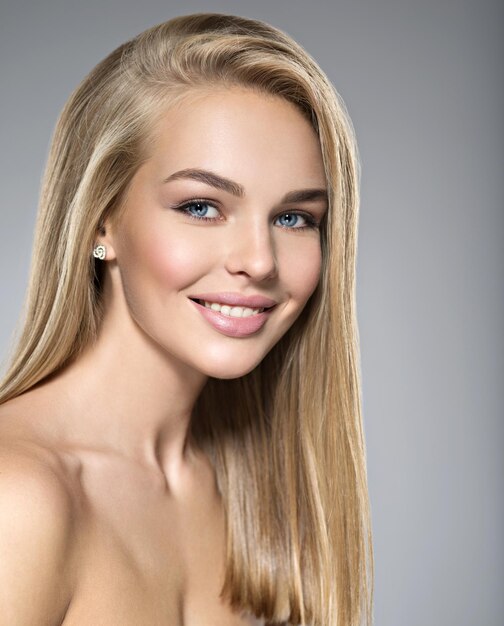 Porträt der jungen Frau mit dem schönen Lächeln. Hübsches wunderschönes Mädchen mit langen hellen glatten Haaren und braunem Make-up. Gesicht eines Modells blaue Augen. posieren