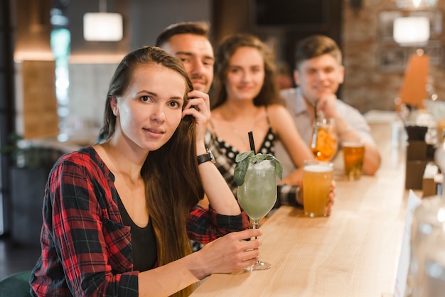 Porträt der jungen Frau mit ihren Freunden, die am Barzähler hält Getränke sitzen