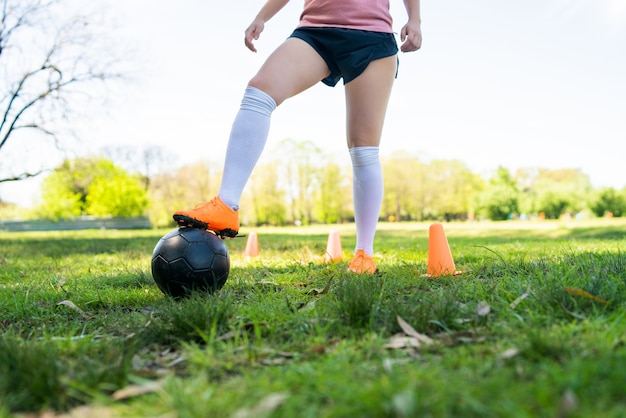 Porträt der jungen Fußballspielerin, die um Kegel läuft, während mit Ball auf dem Feld übt