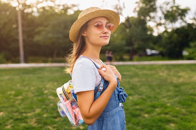 Porträt der jungen hübschen lächelnden Frau im Strohhut und in der rosa Sonnenbrille, die im Park, Sommermodeart, buntes Hipster-Outfit gehen