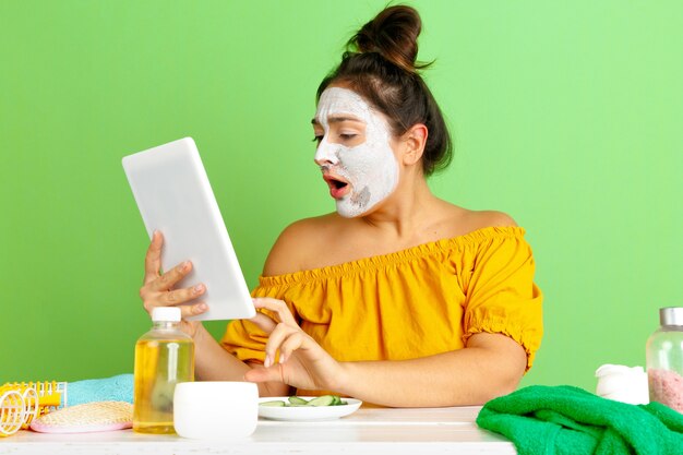 Porträt der jungen kaukasischen Frau im Schönheitstag, Haut- und Haarpflege-Routine. Weibliches Modell, das Selfie, Vlog oder Videoanruf macht, während Gesichtsmaske angewendet wird. Selbstpflege-, Naturschönheits- und Kosmetikkonzept.