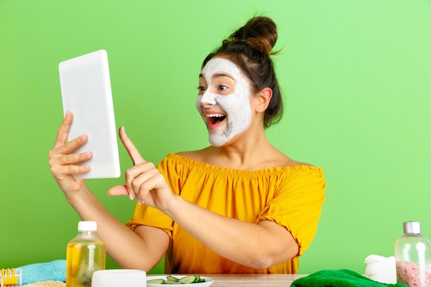 Kostenloses Foto porträt der jungen kaukasischen frau im schönheitstag, haut- und haarpflege-routine. weibliches modell, das selfie, vlog oder videoanruf macht, während gesichtsmaske angewendet wird. selbstpflege-, naturschönheits- und kosmetikkonzept.