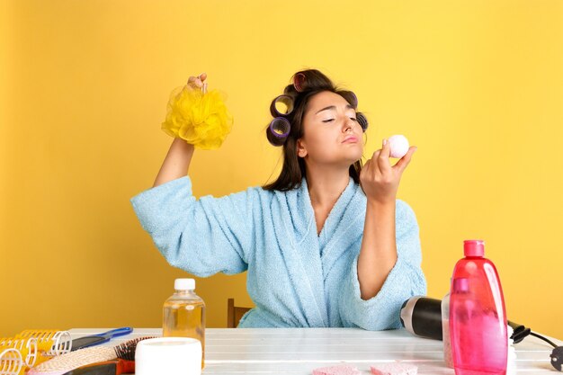 Porträt der jungen kaukasischen Frau in ihrem Schönheitstag, Haut- und Haarpflege-Routine. Weibliches Modell mit Naturkosmetik, die Creme und Öle für Make-up aufträgt. Körper- und Gesichtspflege, natürliches Schönheitskonzept.