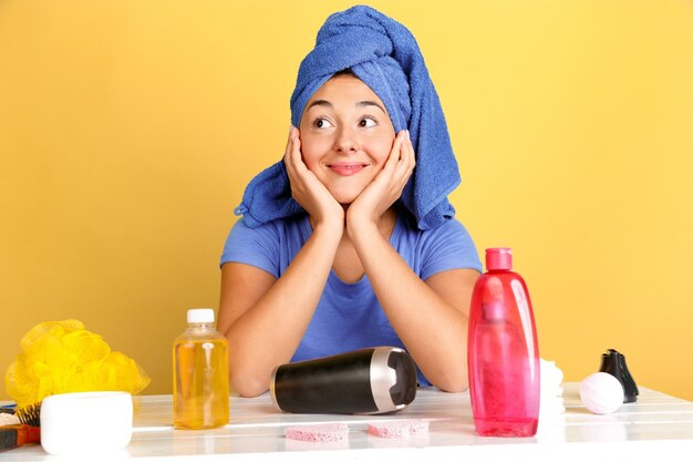 Porträt der jungen kaukasischen Frau in ihrem Schönheitstag, Haut- und Haarpflege-Routine. Weibliches Modell mit Naturkosmetik, die Creme und Öle für Make-up aufträgt. Körper- und Gesichtspflege, natürliches Schönheitskonzept.