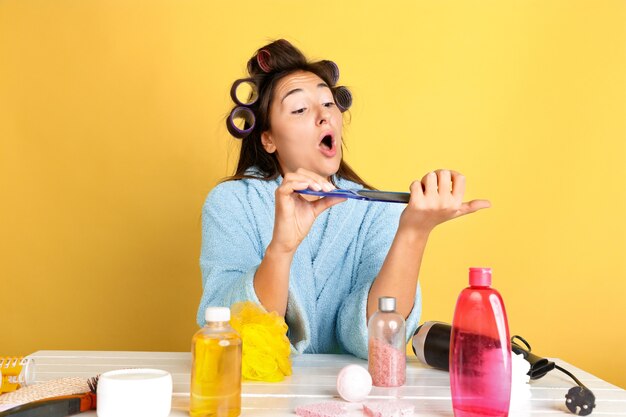 Porträt der jungen kaukasischen Frau in ihrem Schönheitstag, Haut- und Haarpflege-Routine. Weibliches Modell mit Naturkosmetik, die Creme und Öle für Make-up aufträgt. Körper- und Gesichtspflege, natürliches Schönheitskonzept.