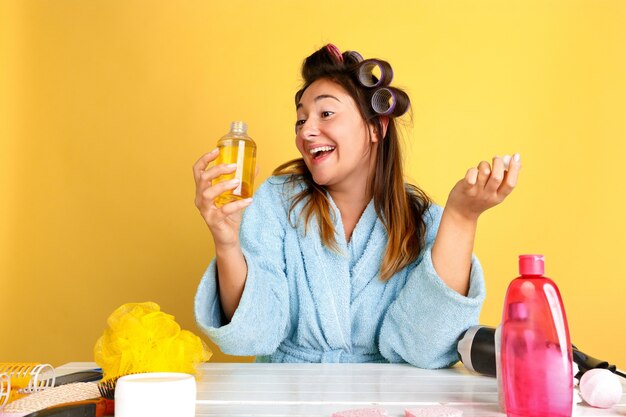 Porträt der jungen kaukasischen Frau in ihrem Schönheitstag, Haut- und Haarpflege-Routine. Weibliches Modell mit Naturkosmetik, die Creme und Öle für Make-up aufträgt. Körper- und Gesichtspflege, natürliches Schönheitskonzept.