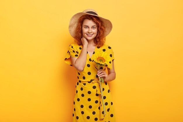 Porträt der jungen rothaarigen Frau, die im gelben Polka-Kleid und im Strohhut aufwirft