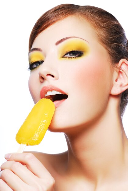 Porträt der jungen schönen Frau der Sinnlichkeit, die gelbes süßes Eis isst