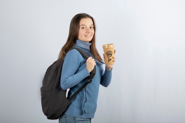 Porträt der jungen schönen Frau mit dem Rucksack, der eine Tasse Kaffee hält.