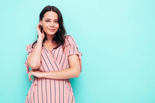 Porträt der jungen schönen lächelnden Frau im trendigen rosa Sommerkleid Sexy sorglose Frau posiert in der Nähe der blauen Wand im Studio Positives Modell, das sich drinnen amüsiert Fröhlich und glücklich