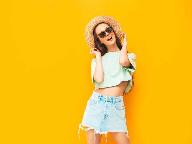 Porträt der jungen schönen lächelnden Frau im trendigen Sommerjeansrock sorglose Frau, die in der Nähe der gelben Wand im Studio posiert Positives Modell, das sich drinnen amüsiert Fröhlich und glücklich In Hut