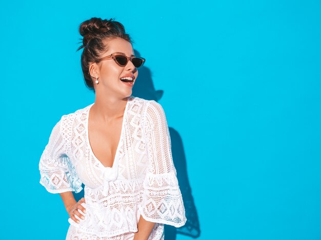 Porträt der jungen schönen sexy lächelnden Frau mit Ghulfrisur. Modisches Mädchen im weißen Hippie-Anzug des zufälligen Sommers kleidet in der Sonnenbrille. Heißes Baumuster getrennt auf Blau