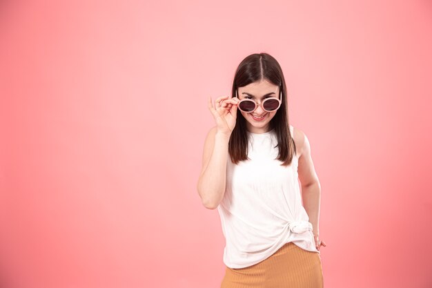 Porträt der jungen stilvollen Frau in der Sonnenbrille mit Lächeln auf Gesicht auf rosa Hintergrund lokalisierten Kopienraum.