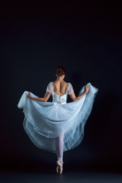 Porträt der klassischen Ballerina im weißen Kleid auf schwarzer Wand