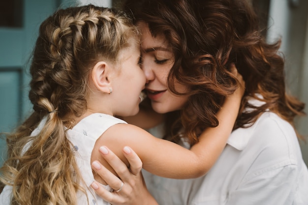 Porträt der kleinen Tochter, die ihre schöne glückliche Mutter küsst