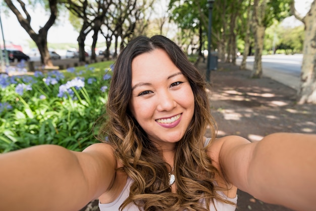 Porträt der lächelnden jungen Frau, die selfie im Park nimmt