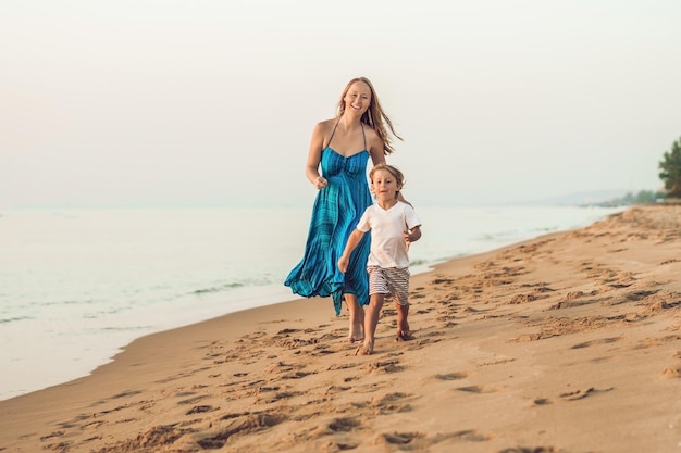 Porträt der lächelnden jungen mutter mit dem kleinen kind, das am strand läuft.