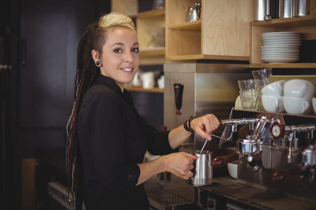 Porträt der lächelnden Kellnerin, welche die Kaffeemaschine verwendet