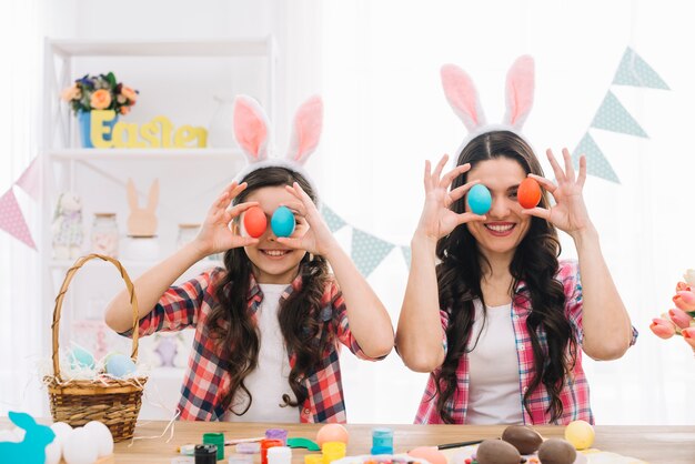 Porträt der lächelnden Mutter und ihrer Tochter, die ihre Augen mit Ostereiern bedecken