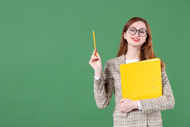 Porträt der Lehrerin posiert mit gelber Datei und Bleistift lächelnd auf Grün