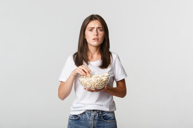 Porträt der mitfühlenden jungen Frau, die herzerwärmenden Film sieht, Popcorn isst.