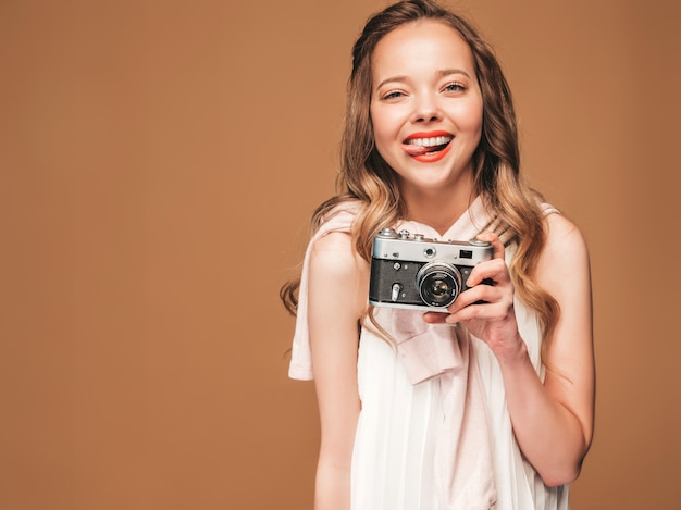 Porträt der netten jungen Frau, die Foto mit Inspiration macht und weißes Kleid trägt. Mädchen, das Retro- Kamera anhält. Model posiert