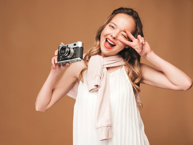 Porträt der netten jungen Frau, die Foto mit Inspiration macht und weißes Kleid trägt. Mädchen, das Retro- Kamera anhält. Model posiert