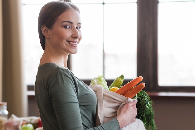 Porträt der positiven Frau, die Tasche mit frischen Lebensmitteln hält
