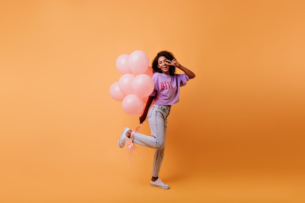 Porträt der raffinierten afrikanischen Frau in voller Länge, die sich auf das Ereignis vorbereitet. verträumte Geburtstagskind tanzen mit Luftballons.