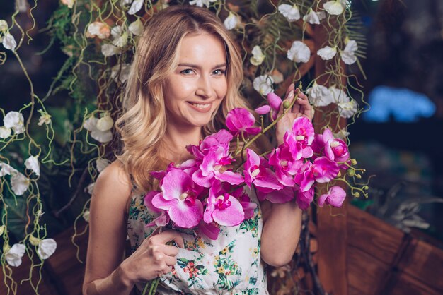 Porträt der recht jungen Frau, die in der Hand rosa Orchideen hält