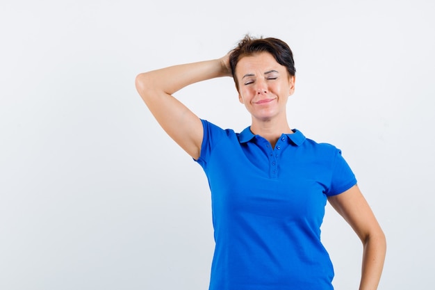 Porträt der reifen Frau, die Hand hinter Kopf im blauen T-Shirt hält und friedliche Vorderansicht schaut