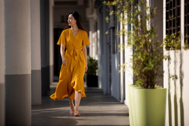 Porträt der schönen asiatischen Frau im gelben Kleid, die draußen in der Stadt aufwirft