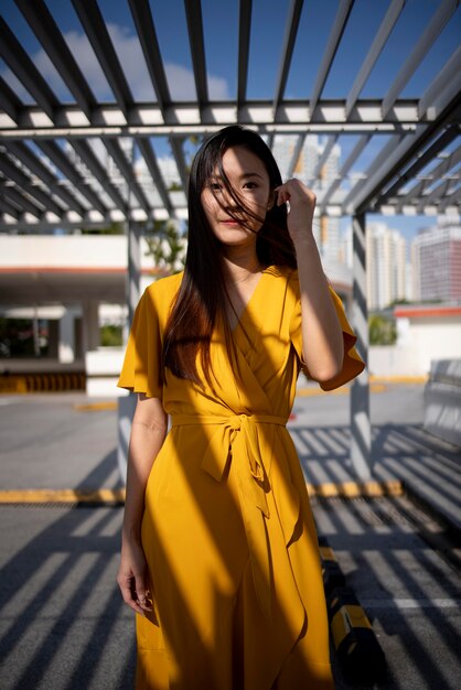 Porträt der schönen asiatischen Frau im gelben Kleid, die draußen in der Stadt aufwirft