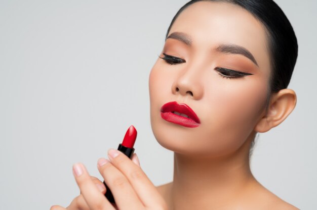 Porträt der schönen asiatischen Frau mit Lippenstift in der Hand