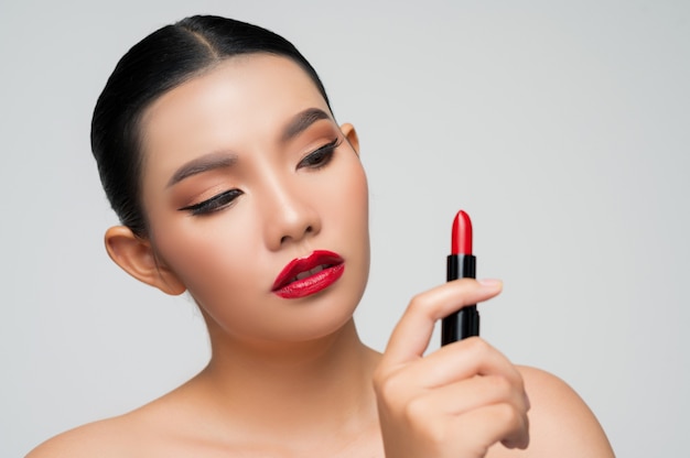 Porträt der schönen asiatischen Frau mit Lippenstift in der Hand