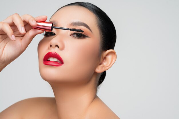 Porträt der schönen asiatischen Frau mit Wimperntusche in der Hand