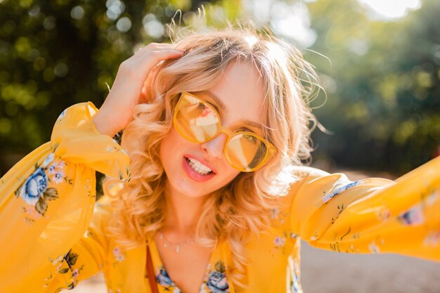 Porträt der schönen blonden stilvollen lächelnden Frau in der gelben Bluse, die Sonnenbrille trägt, die selfie Foto macht